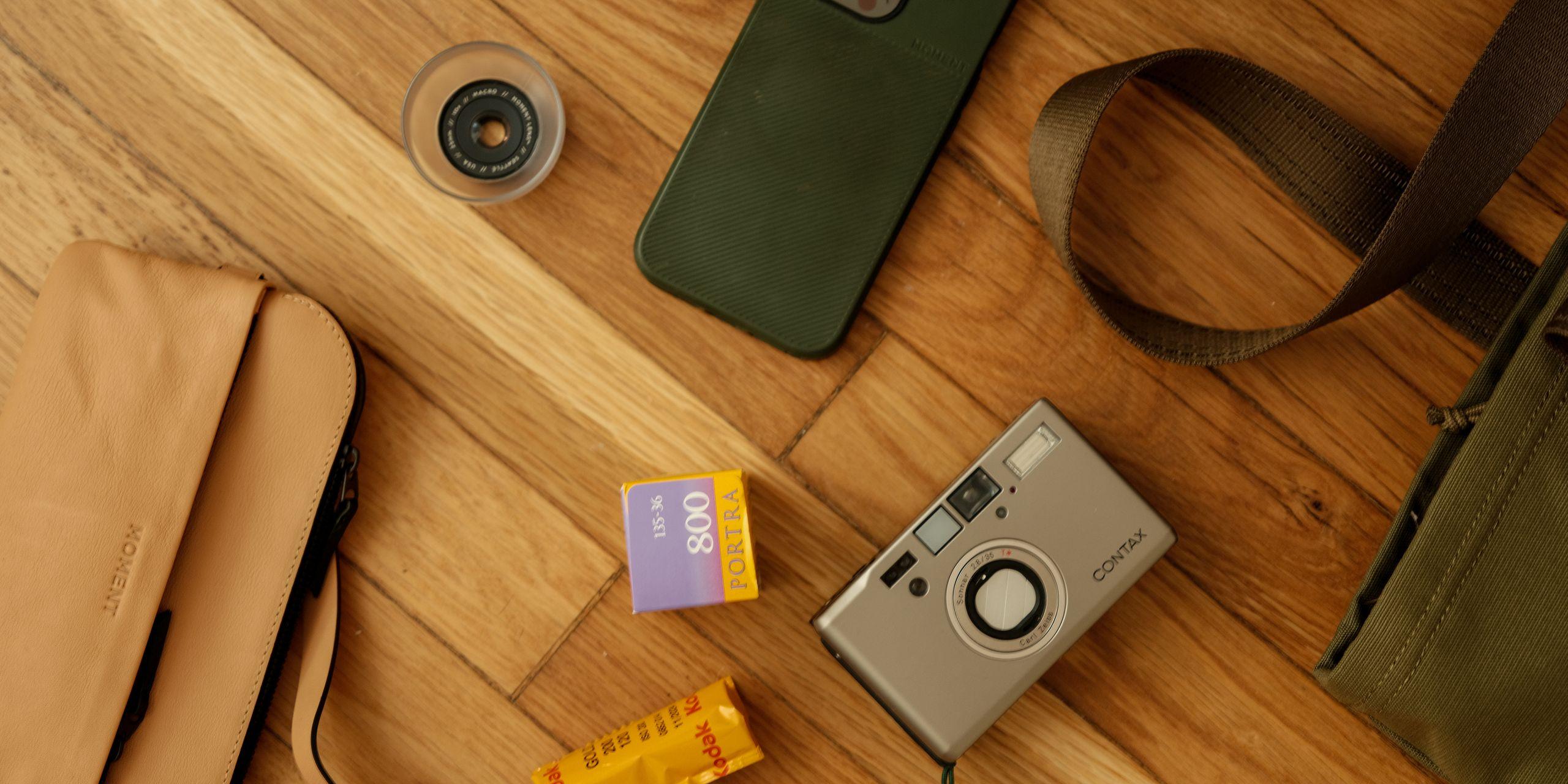 A flatlay image of a Contax T3, sunglasses, Moment lenses, and a green tote.